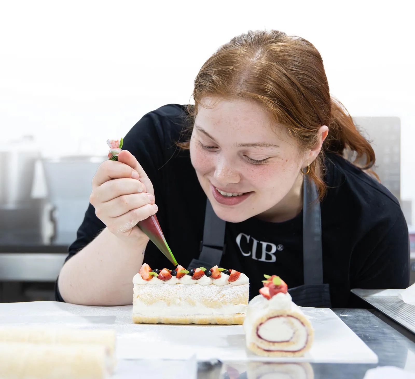 A CIB pastry student pipes cream onto a strawberry-topped roll cake